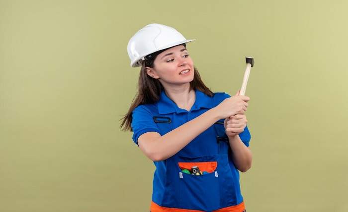 scared young builder girl with white safety helmet blue uniform holds hammer with both hands isolated green background 141793 34534